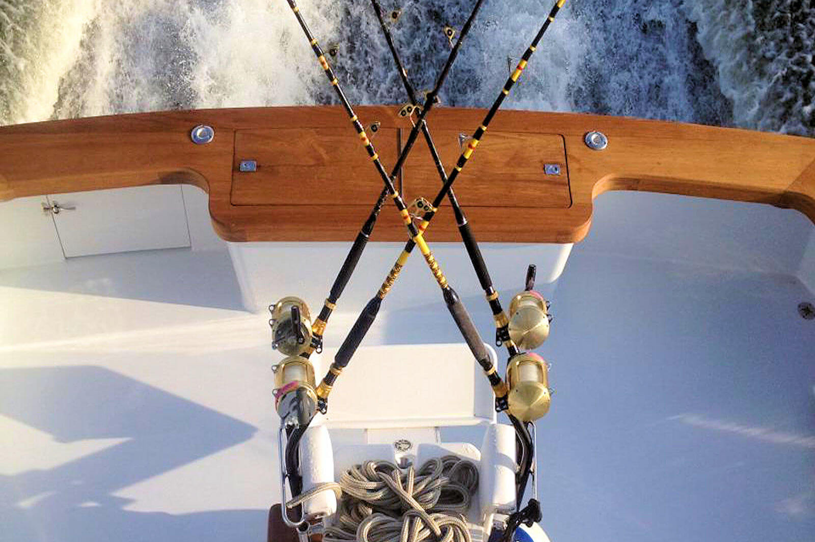  water is visible in the background. Four fishing rods, with gold reels, are arranged in an X shape on the boat's deck, secured in holders. 